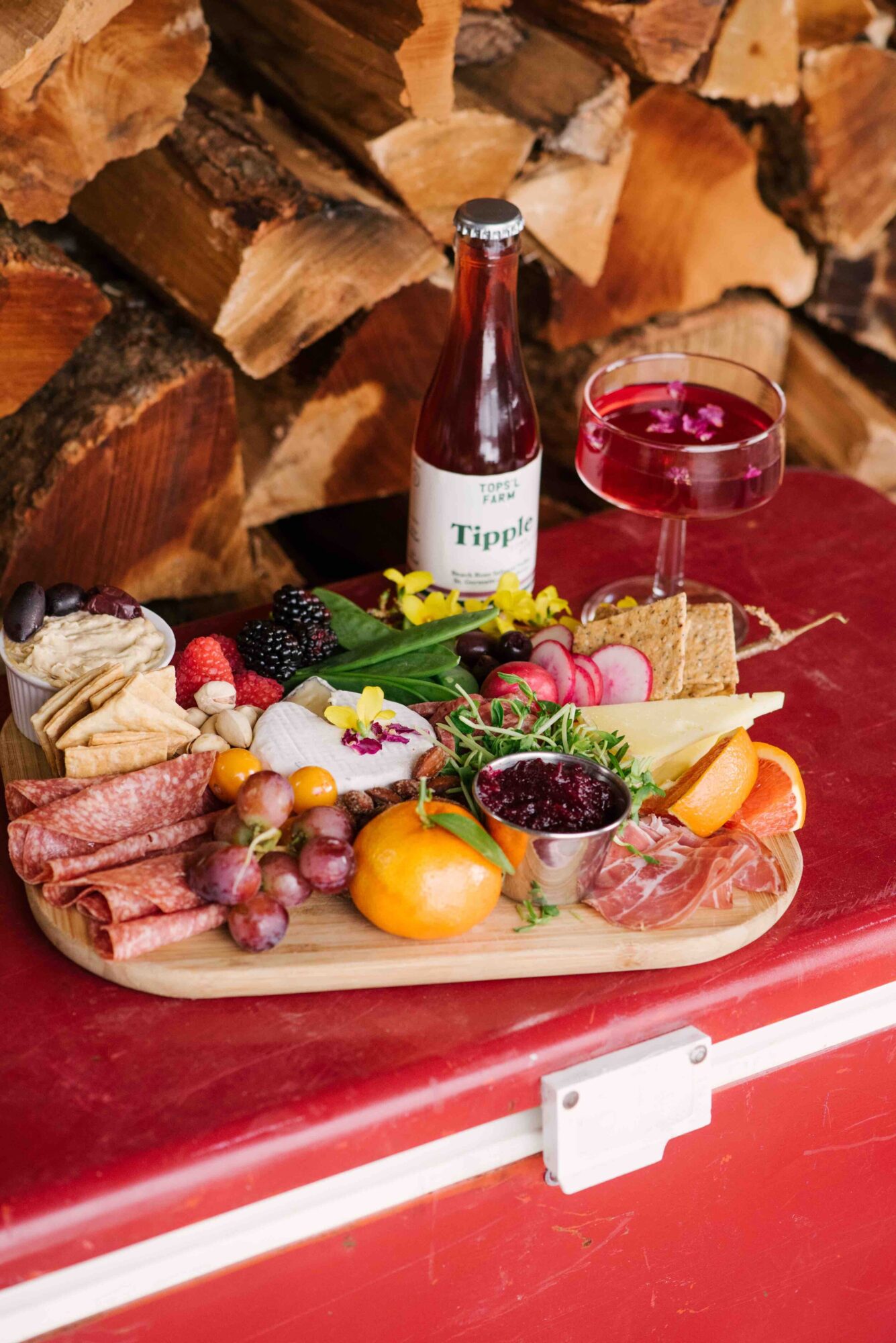 Local cheese, cured meats, and fermented vegetables are paired with artisanal crackers, seasonal fruits, and floral garnishes to create an opulent picnic cheese board.